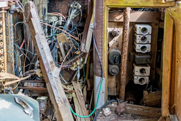 Verfallene Steuerungseinheit einer alten Straßenbahn mit freiliegenden Kabeln, Schaltern und verrosteten Metallteilen in einem engen Raum