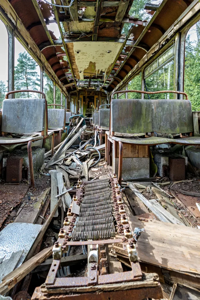 Innenraum einer verfallenen Straßenbahn mit beschädigtem Dach, rostigen Sitzgestellen und Trümmern auf dem Boden