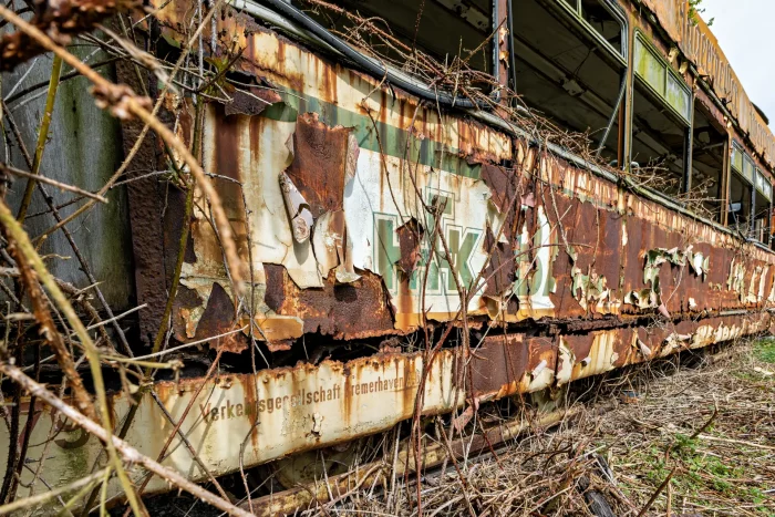 Verfallene Straßenbahn mit abgeblättertem Lack, Roststellen und verblasster Schrift in überwucherter Umgebung