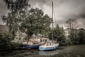 Zwei Boote liegen an einem bewachsenen Ufer unter bewölktem Himmel