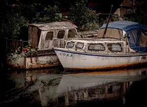 Zwei alte Boote am Ufer, eines mit dem Namen 'CORA' auf dem Bug, das andere mit einer verwitterten Kabine