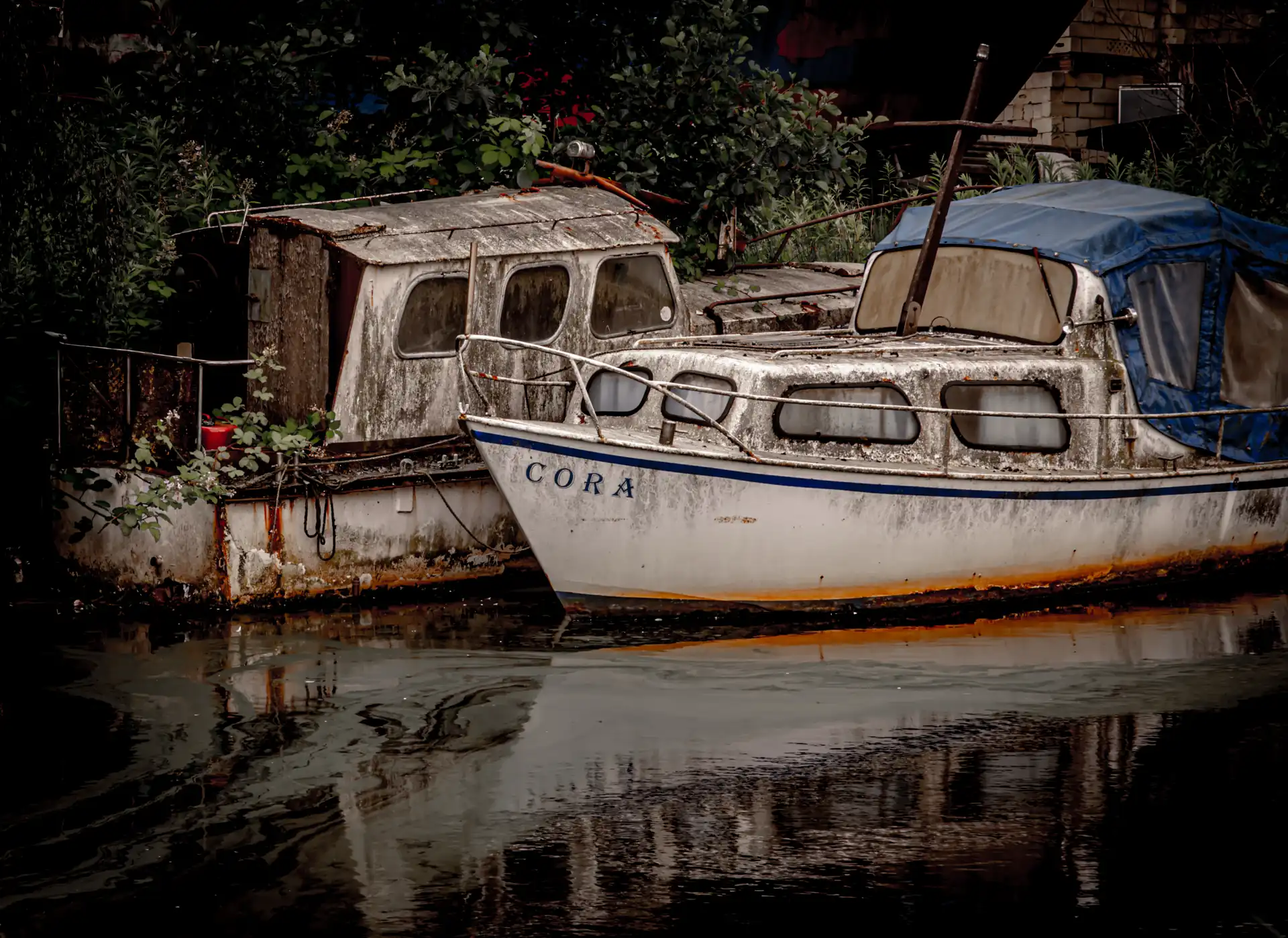 Zwei alte Boote am Ufer, eines mit dem Namen 'CORA' auf dem Bug, das andere mit einer verwitterten Kabine