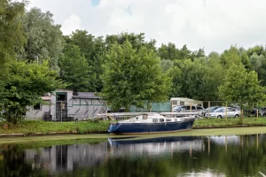 Segelboot am Ufer eines ruhigen Gewässers vor Bäumen, Wohnwagen und parkenden Autos