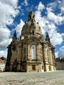 Frauenkirche Dresden von unten fotografiert, markante Kuppel vor Wolkenhimmel, Banner an Fassade.