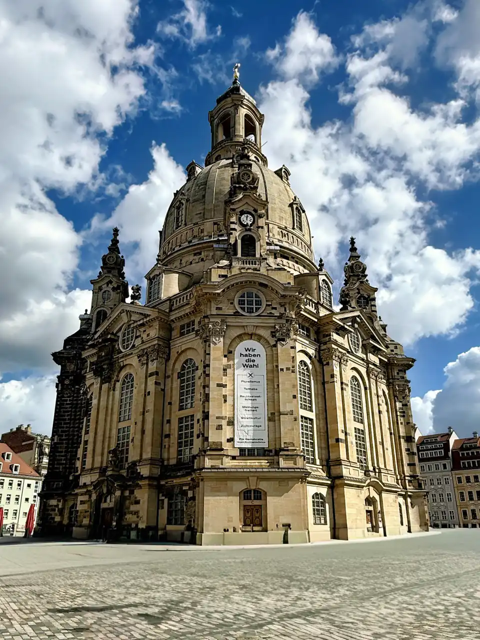 Frauenkirche Dresden von unten fotografiert, markante Kuppel vor Wolkenhimmel, Banner an Fassade.