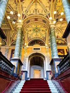 runktreppe mit rotem Läufer im Opernhaus, reich verzierte goldene Decke und Marmorsäulen.