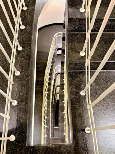 lick von oben in spiralförmiges Treppenhaus mit hellen Handläufen und Metallgeländer.