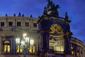 Eckansicht der Semperoper bei Nacht mit Laternenkandelaber und Reiterstatue auf dem Dach.