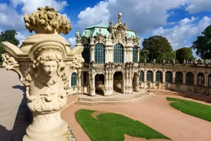 winger-Pavillon mit grünem Kuppeldach, Steinvase mit Frauenkopf im Vordergrund, Rasenornamente.