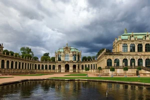 Zwinger-Pavillon mit grünen Kuppeln, gespiegelt im Wasserbecken, dramatische Gewitterwolken im Hintergrund.