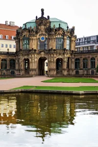 Zwinger-Wallpavillon mit Uhr und geschwungenem Dach, Spiegelung im Teich, Rasenflächen davor.